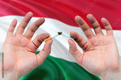 Hungary quit smoking cigarettes concept. Adult man hands breaking cigarette. National health theme and country flag background.