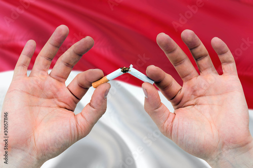 Indonesia quit smoking cigarettes concept. Adult man hands breaking cigarette. National health theme and country flag background.