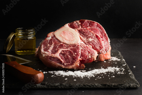 Osobuco carne cruda vista de frente sobre laja negra y fondo negro. Vista de frente y de cerca
