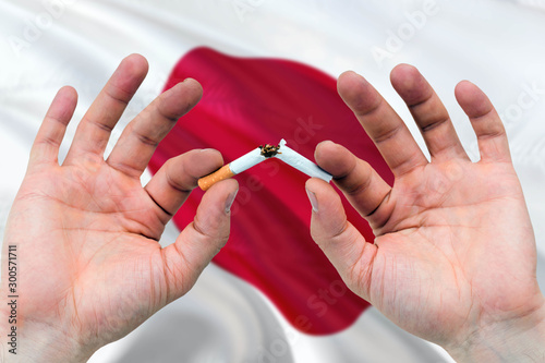 Japan quit smoking cigarettes concept. Adult man hands breaking cigarette. National health theme and country flag background.