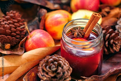 Autumn sangria with apples and cinnamon, autumn leaves brown color background with pinecone, holiday wine cocktail drinking, copy space