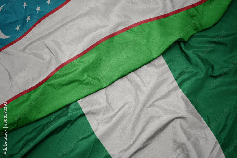 Obraz premium waving colorful flag of nigeria and national flag of uzbekistan.