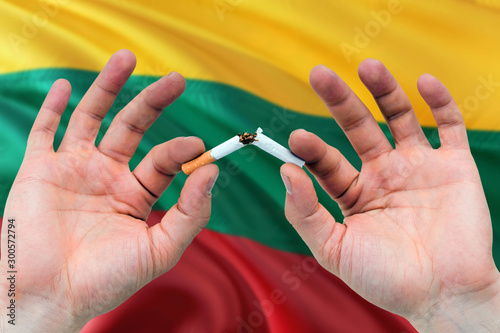 Lithuania quit smoking cigarettes concept. Adult man hands breaking cigarette. National health theme and country flag background.