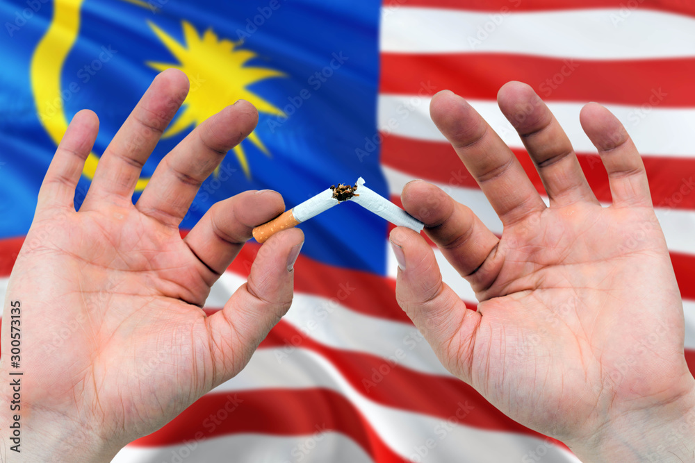 Malaysia quit smoking cigarettes concept. Adult man hands breaking cigarette. National health theme and country flag background. Malaysia quit smoking cigarettes concept. Adult man hands breaking cigarette. National health theme and country flag background.