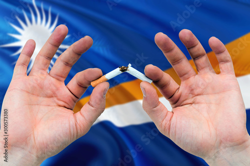 Marshall Islands quit smoking cigarettes concept. Adult man hands breaking cigarette. National health theme and country flag background.