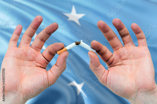 Micronesia quit smoking cigarettes concept. Adult man hands breaking cigarette. National health theme and country flag background.