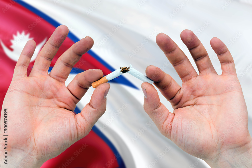 Nepal quit smoking cigarettes concept. Adult man hands breaking cigarette. National health theme and country flag background. Nepal quit smoking cigarettes concept. Adult man hands breaking cigarette. National health theme and country flag background.