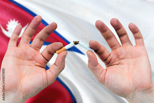 Nepal quit smoking cigarettes concept. Adult man hands breaking cigarette. National health theme and country flag background.