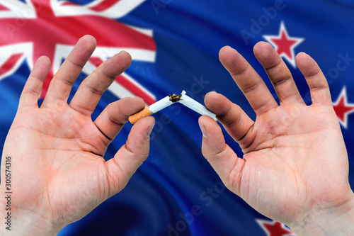 New Zealand quit smoking cigarettes concept. Adult man hands breaking cigarette. National health theme and country flag background.