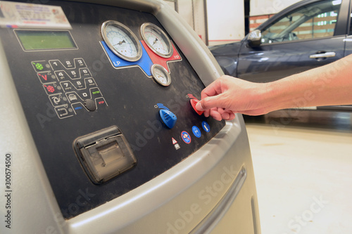 the hand of technician  pull a button of  the car's air conditioning service tool with functional button on the black panel at car service shop near the black car