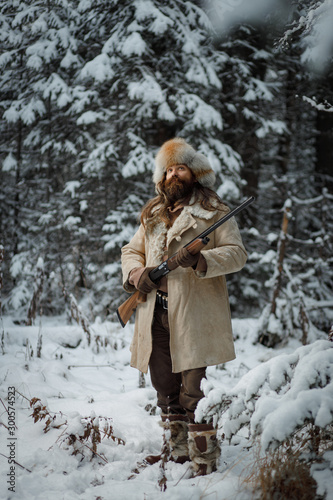 Hunter man in winter warm vintage clothes with gun in winter forest