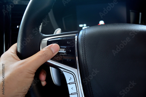 adult hand holding the steering wheel with multi media controler button inside of new car passenger room