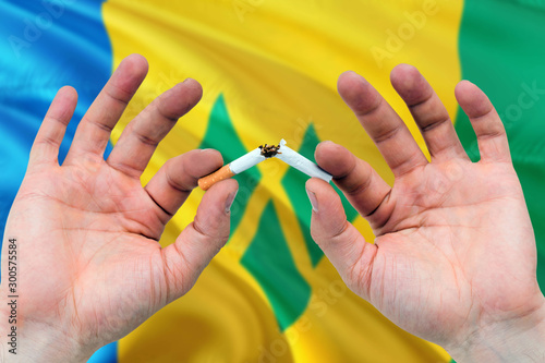 Saint Vincent And The Grenadines quit smoking cigarettes concept. Adult man hands breaking cigarette. National health theme and country flag background.