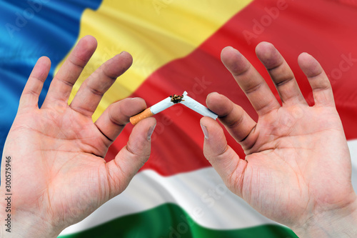 Seychelles quit smoking cigarettes concept. Adult man hands breaking cigarette. National health theme and country flag background.