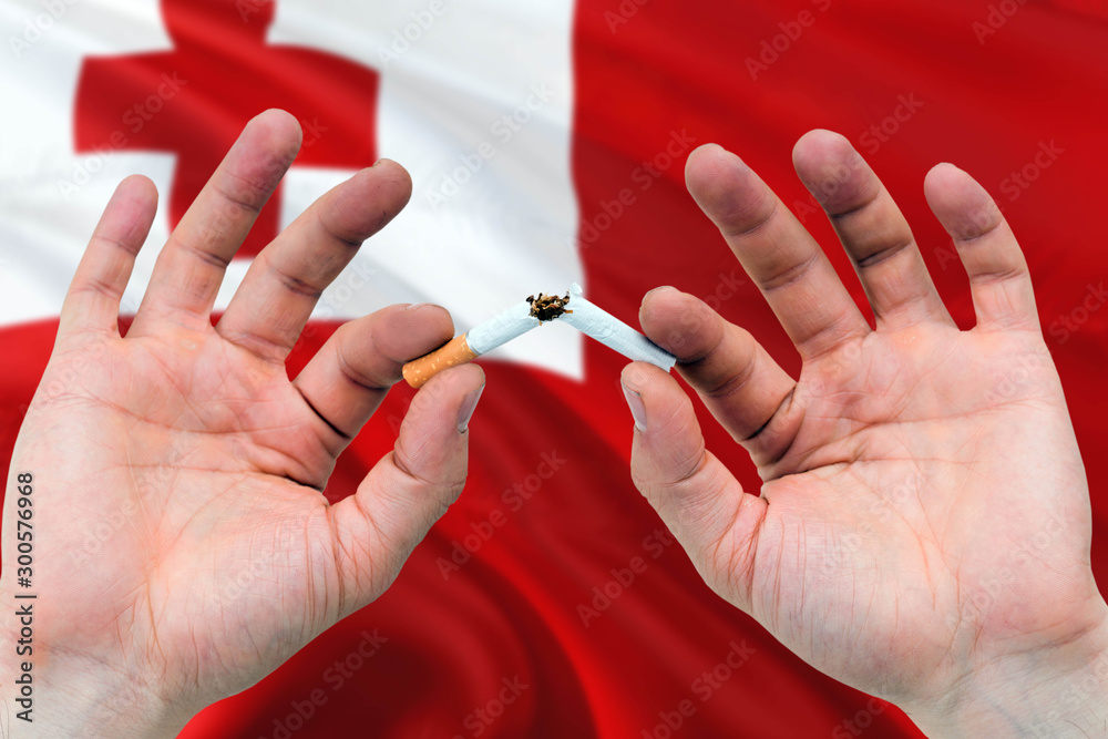 Tonga quit smoking cigarettes concept. Adult man hands breaking cigarette. National health theme and country flag background. Tonga quit smoking cigarettes concept. Adult man hands breaking cigarette. National health theme and country flag background.