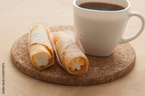 Sweet snack with coffee and waffle tubes on wood background