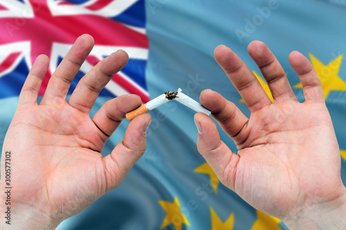 Tuvalu quit smoking cigarettes concept. Adult man hands breaking cigarette. National health theme and country flag background.