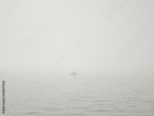 Obraz na plátně fisherman in a boat on a lake in a thick fog catches fish with a fishing rod