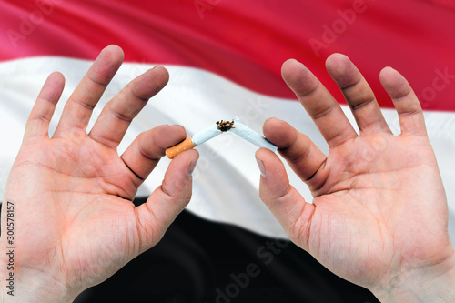 Yemen quit smoking cigarettes concept. Adult man hands breaking cigarette. National health theme and country flag background.