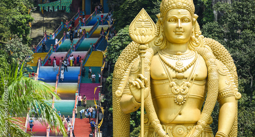 (Selective focus) Stunning view of the  Lord Murugan statue in the foreground and tourists climbing a colorful stairs leading to the Batu Caves in the background. Kuala Lumpur, Malaysia photo