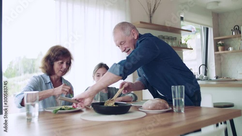 A small girl with senior grandparents indoors sitting at the table, eating. photo