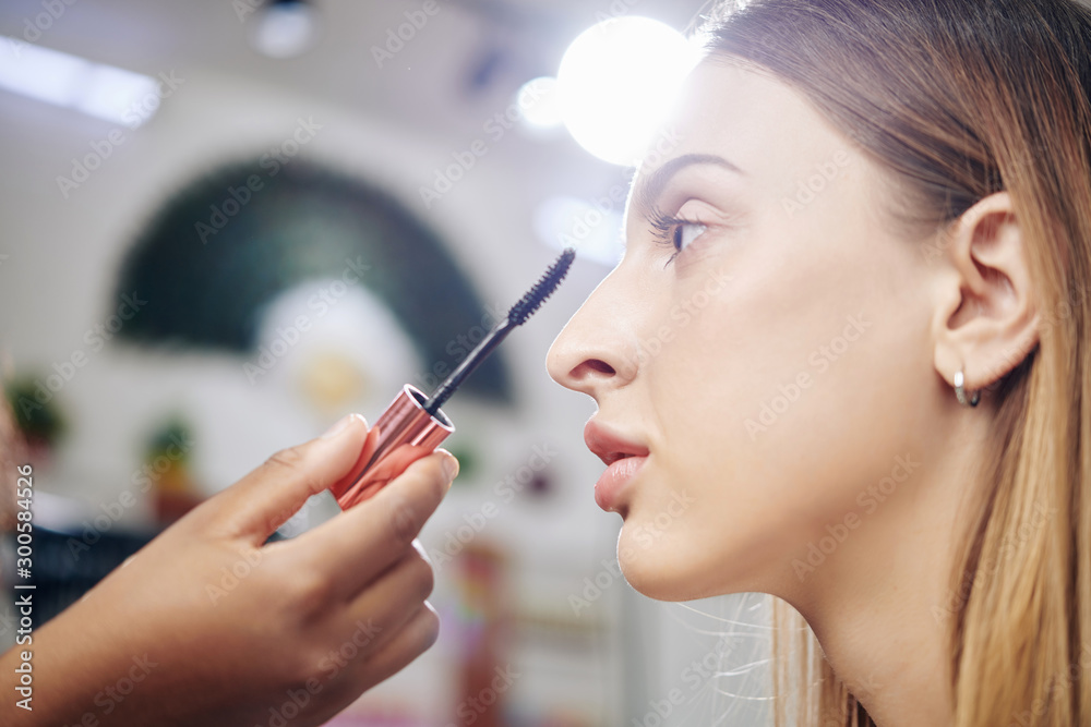 Professional make-up artist applying lengthening mascara to young gorgeous fashion model - obrazy, fototapety, plakaty 