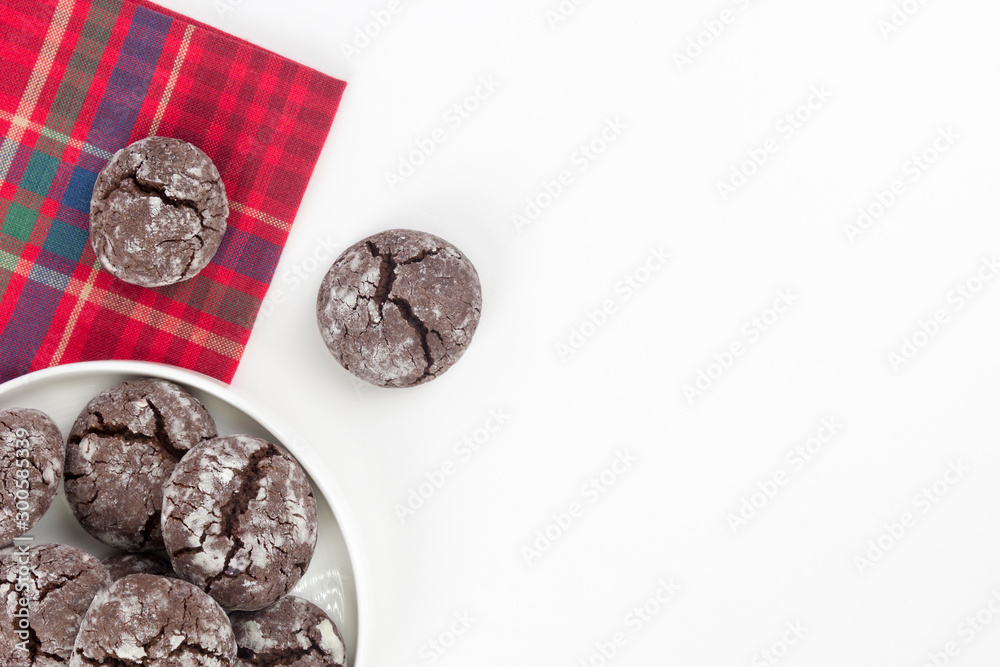 Chocolate crinkle cookies in round plate, red kitchen towel, white background. Christmas, recipe concept. Top view, flat lay, copy space