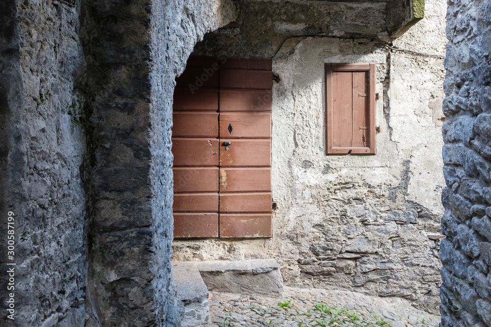 Closed wooden door and a window in a narrow street of a Piedmontese village