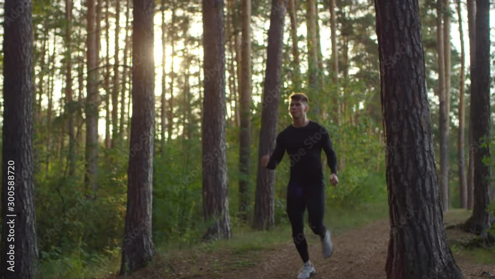 Young Caucasian male athlete in sportswear running on forest trail while exercising in sunny morning Young Caucasian male athlete in sportswear running on forest trail while exercising in sunny morning