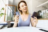 Blonde girl sitting at cafe and keeping leather wallet with debit card.