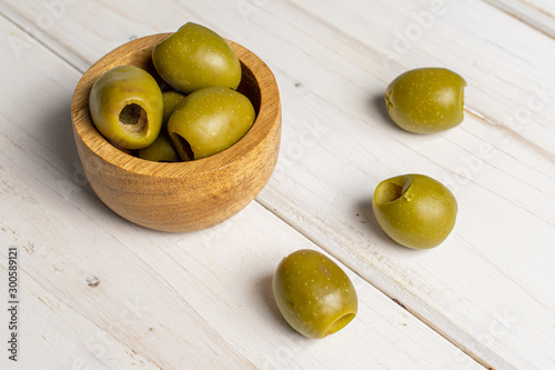 Group of six whole pitted green olive in tiny wooden bowl on white wood photo