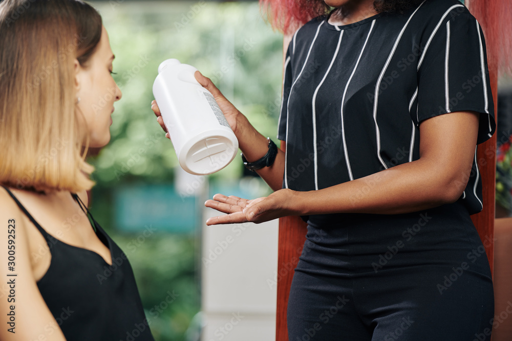 Cropped image hairdresser holding big bottle and describing benefits of new hair treatment to client Cropped image hairdresser holding big bottle and describing benefits of new hair treatment to client