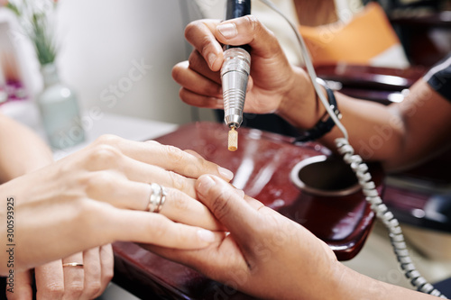 Manicurist using electric nail drill when removing old nail polish  selective focus