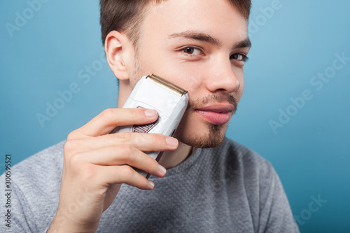 Canvas Print Portrait of happy brunette man with bristle and mustache using epilator to remove facial hair, smiling satisfied with soft skin, male beauty care concept