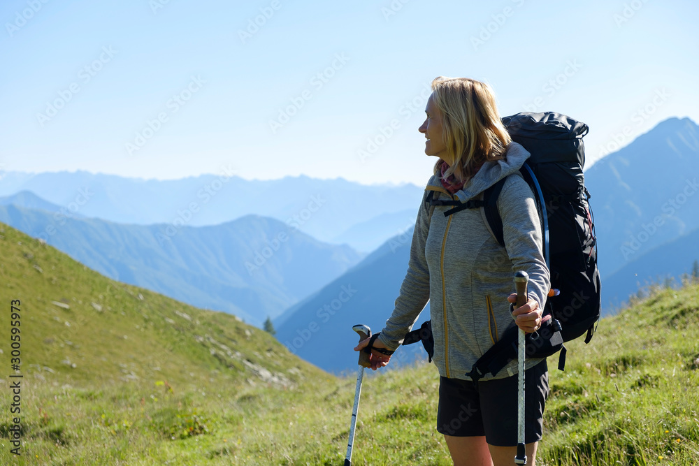 A blonde woman with hiking gear enjoys the view over the mountains of the Italian Alps