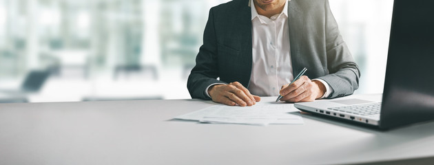 young man in suit writing business papers at desk in modern coworking office. copy space