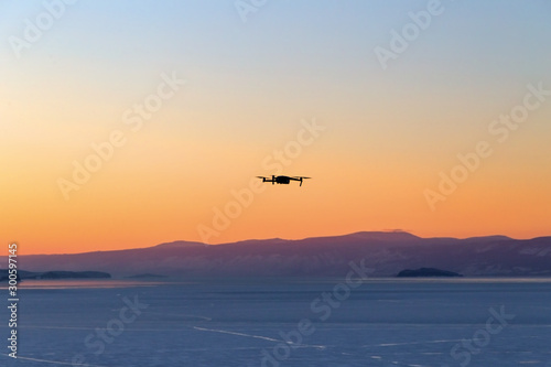 Silhouette of drone flying at sunset on Lake Baikal. Winter time. Photo tour consept
