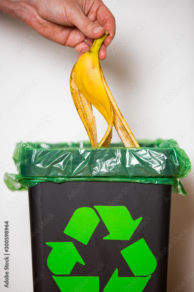 Hand putting banana peel in recycling bio bin. Person in a house