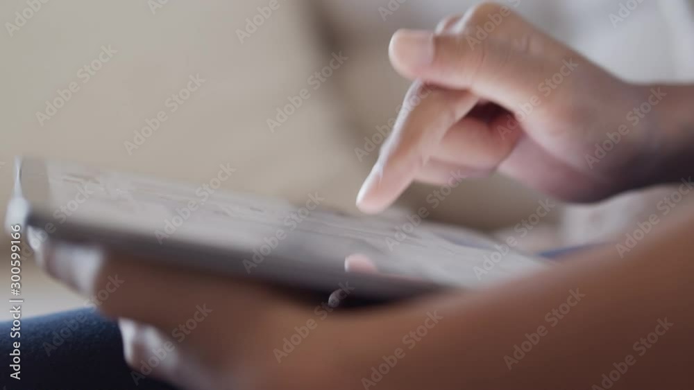 Hand of little girl using  digital tablet to learn while sitting on the sofa in the living room at home