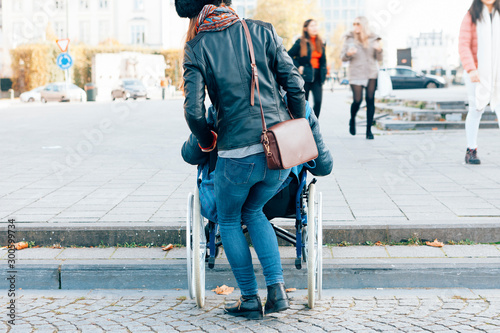 rear view of a woman helping a disabled person to go down the steps with the wheelchair - architectural boundaries in the cities concept