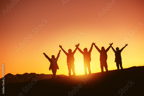 Happy peoples silhouettes against sunset and mountains