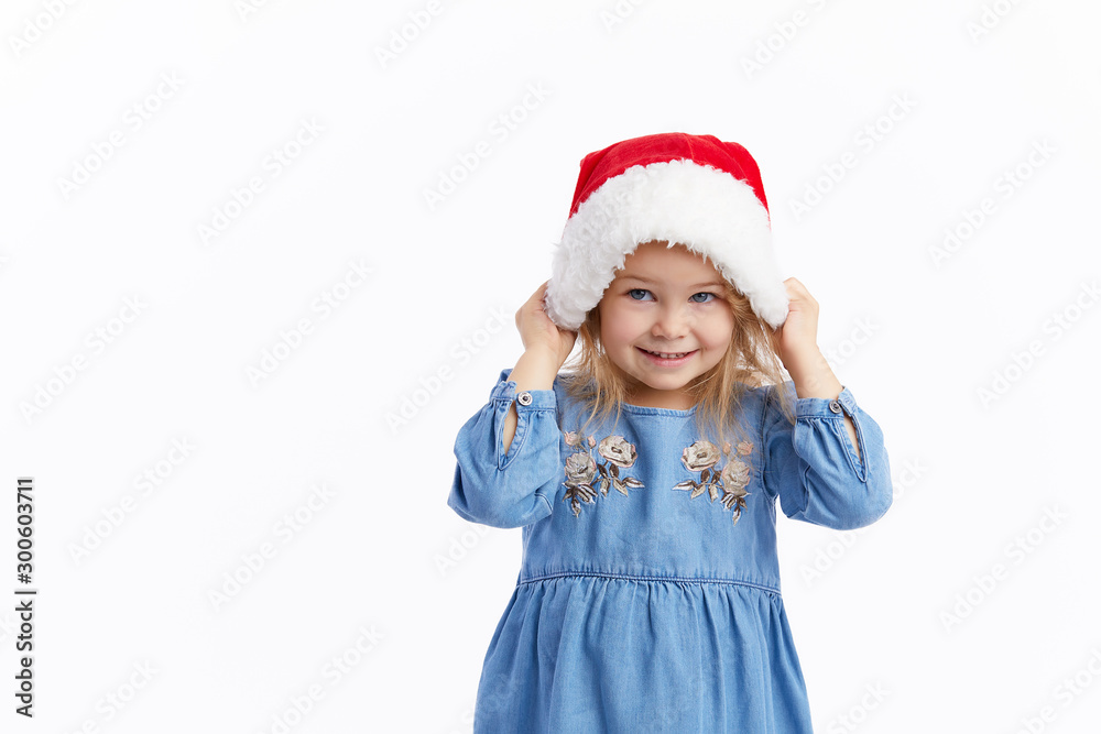 Happy smiling child girl in Santa hat and blue dress having fun on a red isolated background. Merry Christmas. Happy New Year Happy smiling child girl in Santa hat and blue dress having fun on a red isolated background. Merry Christmas. Happy New Year