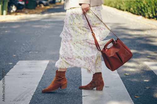fashion blogger street style. fashionable woman posing wearing an oversized blazer, floral vintage dress, suede cowboy ankle boots and a black trendy mini handbag. perfect fall 2019 outfit. 