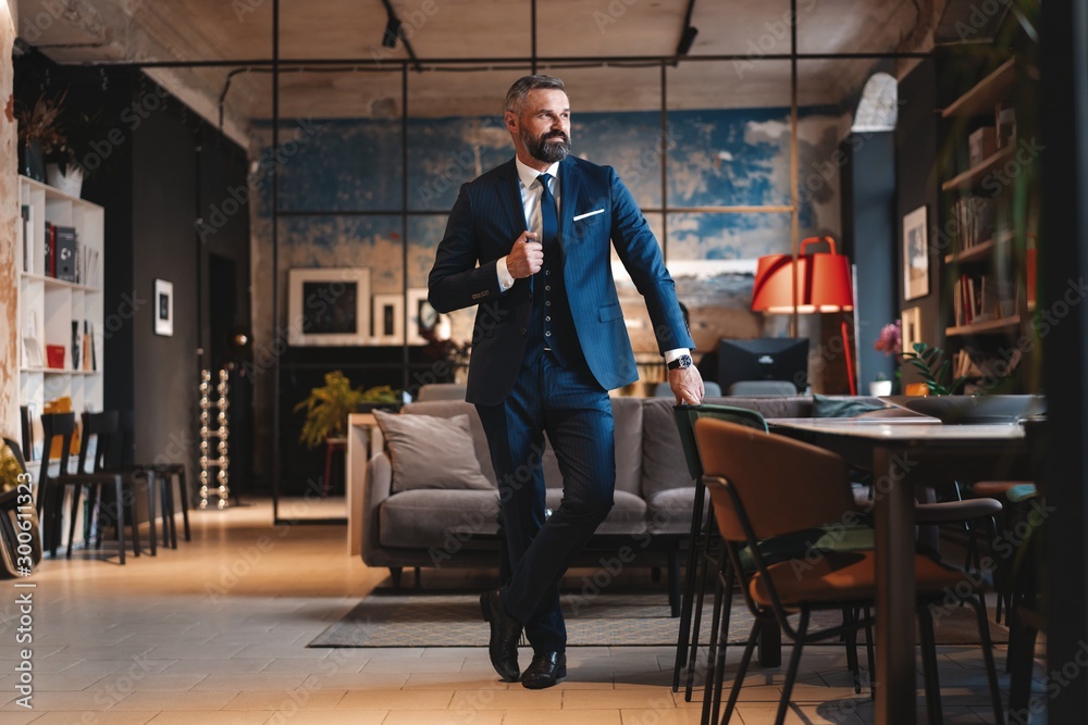 Stylish bearded man in a suit standing in modern office - obrazy, fototapety, plakaty 