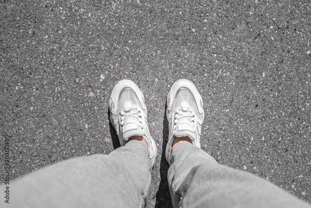 white sneakers walking on concrete. Sneakers on the pavement. Top view of legs on asphalt. white sneakers walking on concrete. Sneakers on the pavement. Top view of legs on asphalt.
