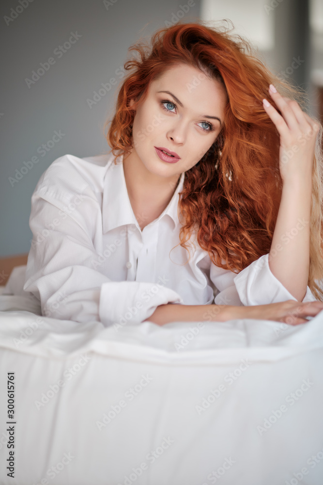 Smiling and looking forward. Hot redhead girl sits on the white bed Smiling and looking forward. Hot redhead girl sits on the white bed