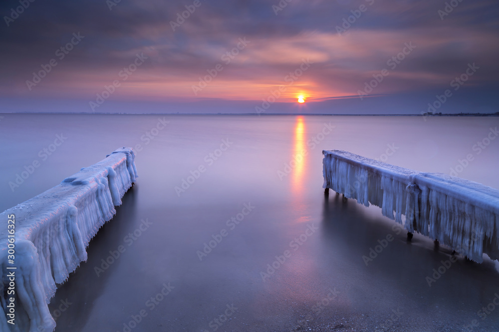 Covered with ice pier in sea at sunset