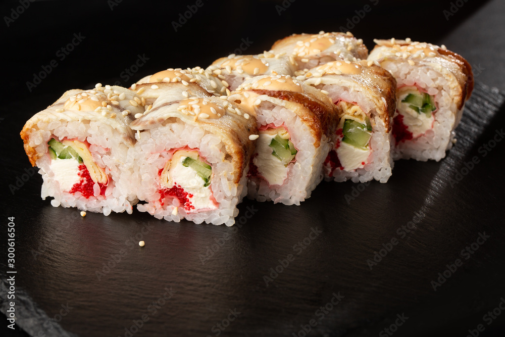 Sushi Rolls with cucumber, flying fish caviar, eel, omelet and Cream Cheese inside on black slate isolated. Philadelphia unagi roll sushi with tamago. Sushi menu. Horizontal photo. Sushi Rolls with cucumber, flying fish caviar, eel, omelet and Cream Cheese inside on black slate isolated. Philadelphia unagi roll sushi with tamago. Sushi menu. Horizontal photo.
