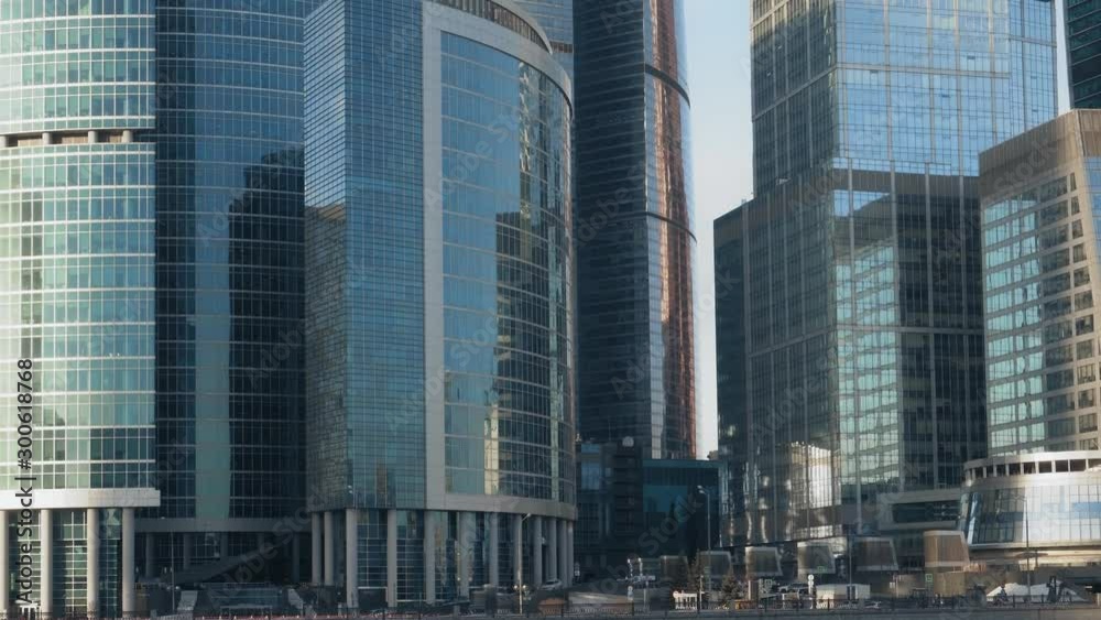 Glass facades of modern futuristic skyscrapers. Close-up. In front of the buildings is an embankment with heavy traffic. Slow and smooth motion of the frame, from the bottom up. Ultra HD stock footage Glass facades of modern futuristic skyscrapers. Close-up. In front of the buildings is an embankment with heavy traffic. Slow and smooth motion of the frame, from the bottom up. Ultra HD stock footage