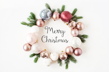 Christmas / New Year holiday composition. Quote "Merry Christmas" in frame wreath with Christmas baubles, balls and fir branches on white background. Flat lay, top view festive concept.